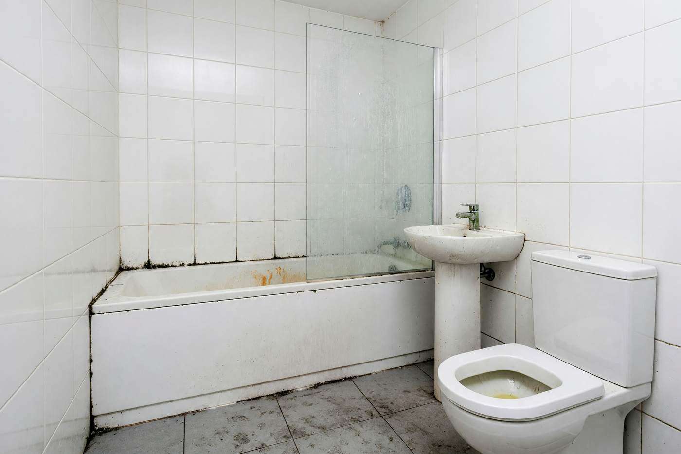 Bathroom with limescale on the shower screen, black mould in the grout and a stained bath